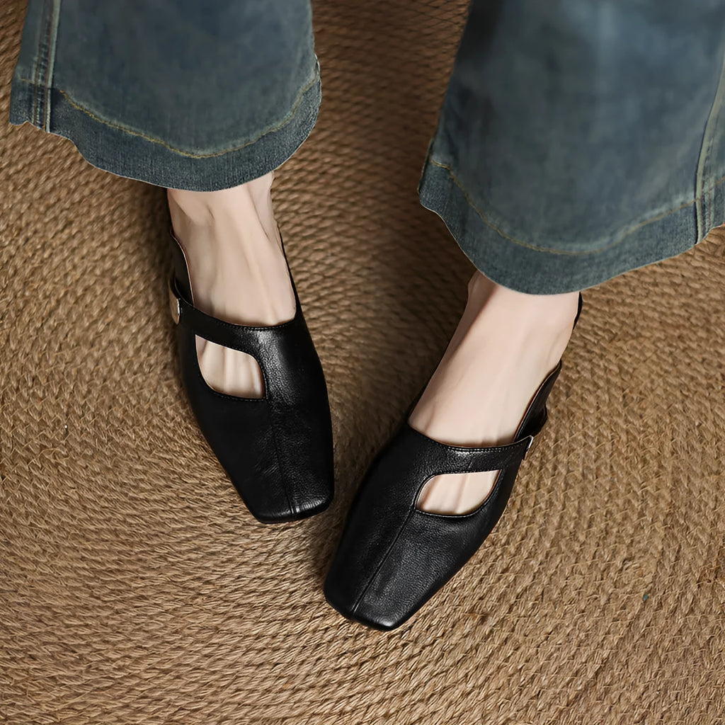 A pair of beige square head low heel slippers with a rubber sole on a wooden deck.