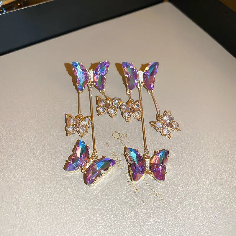 Silver needle style drop earrings with blue purple butterfly, crystals, and a tassel.