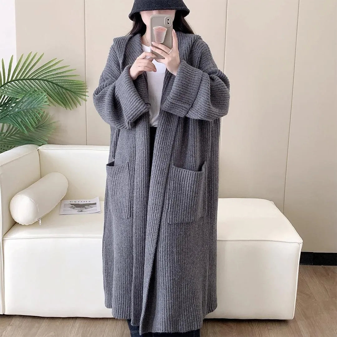 A long, loose grey hooded cardigan coat for women on a hanger, showing its length and raglan sleeves.