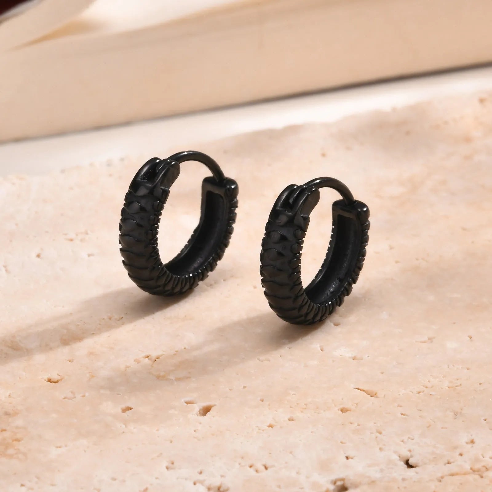 A pair of stainless steel hip hop earrings with a raised snake pattern, shown in black and gold colour options.