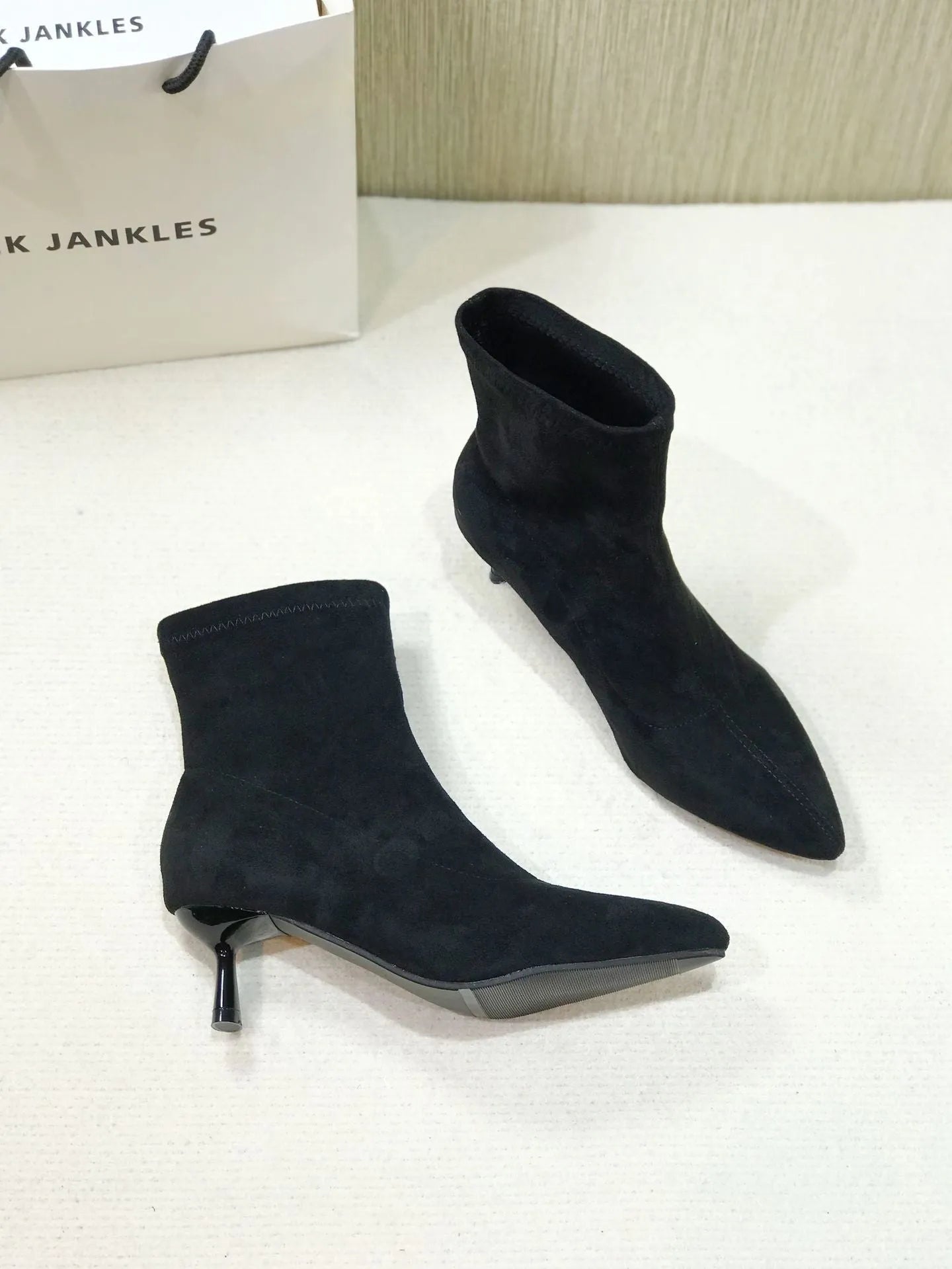 Black pointed toe stiletto ankle boots with a mid-calf sock length on a model.