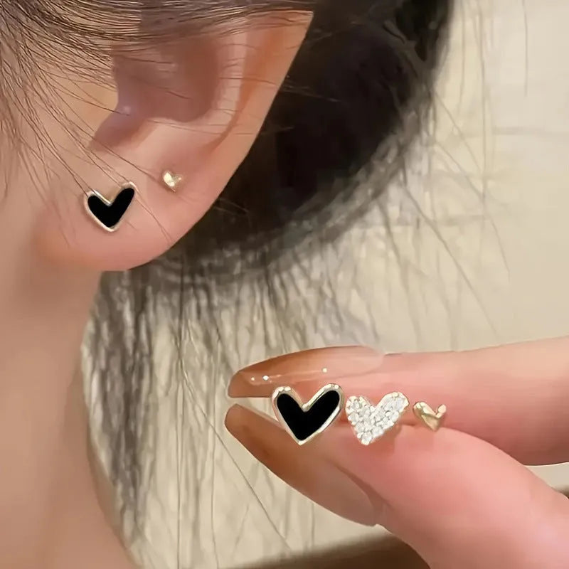Three pairs of heart-shaped alloy earrings in gold, black, black and white, and pink colours