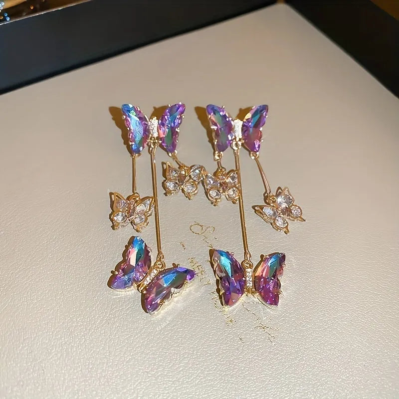 Silver needle style drop earrings with blue purple butterfly, crystals, and a tassel.