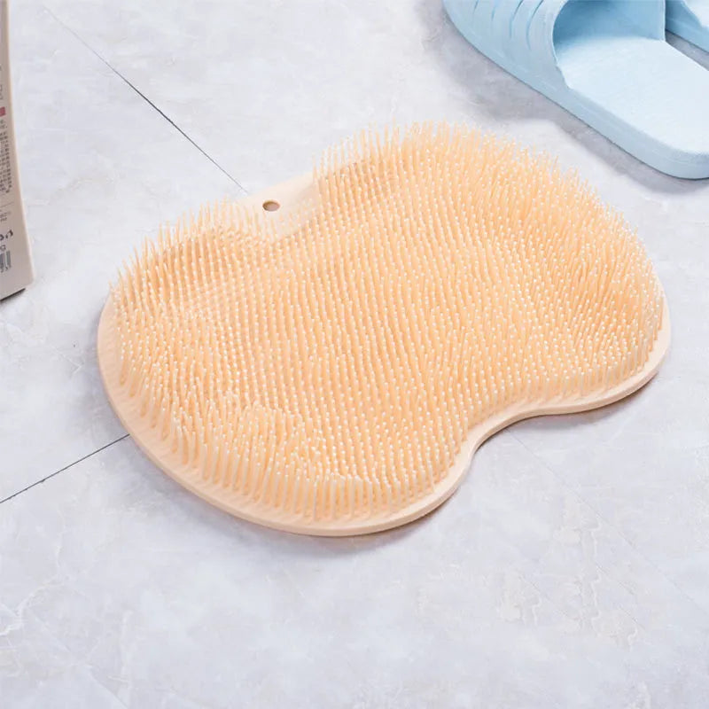 Orange suction cup bath brush with silicone bristles for foot and back cleaning on a bathroom floor.