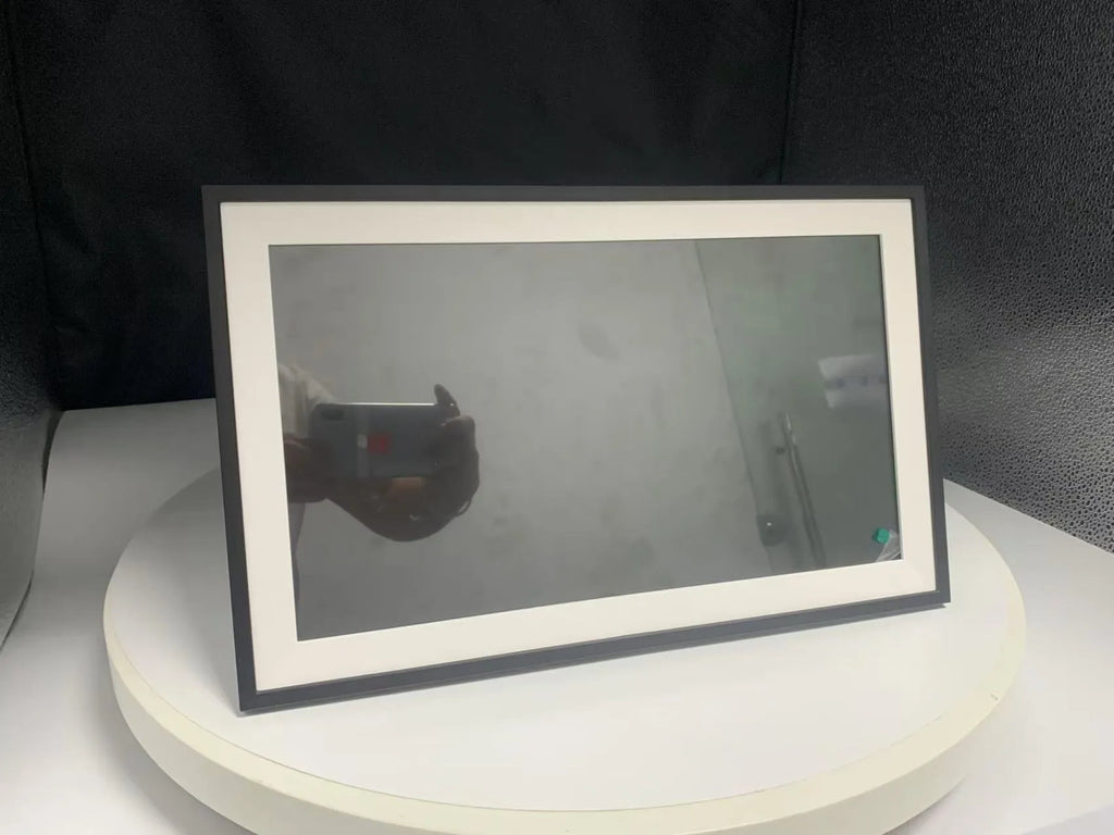White smart digital photo frame with 15.6 inch screen on a table, showing a family photo.