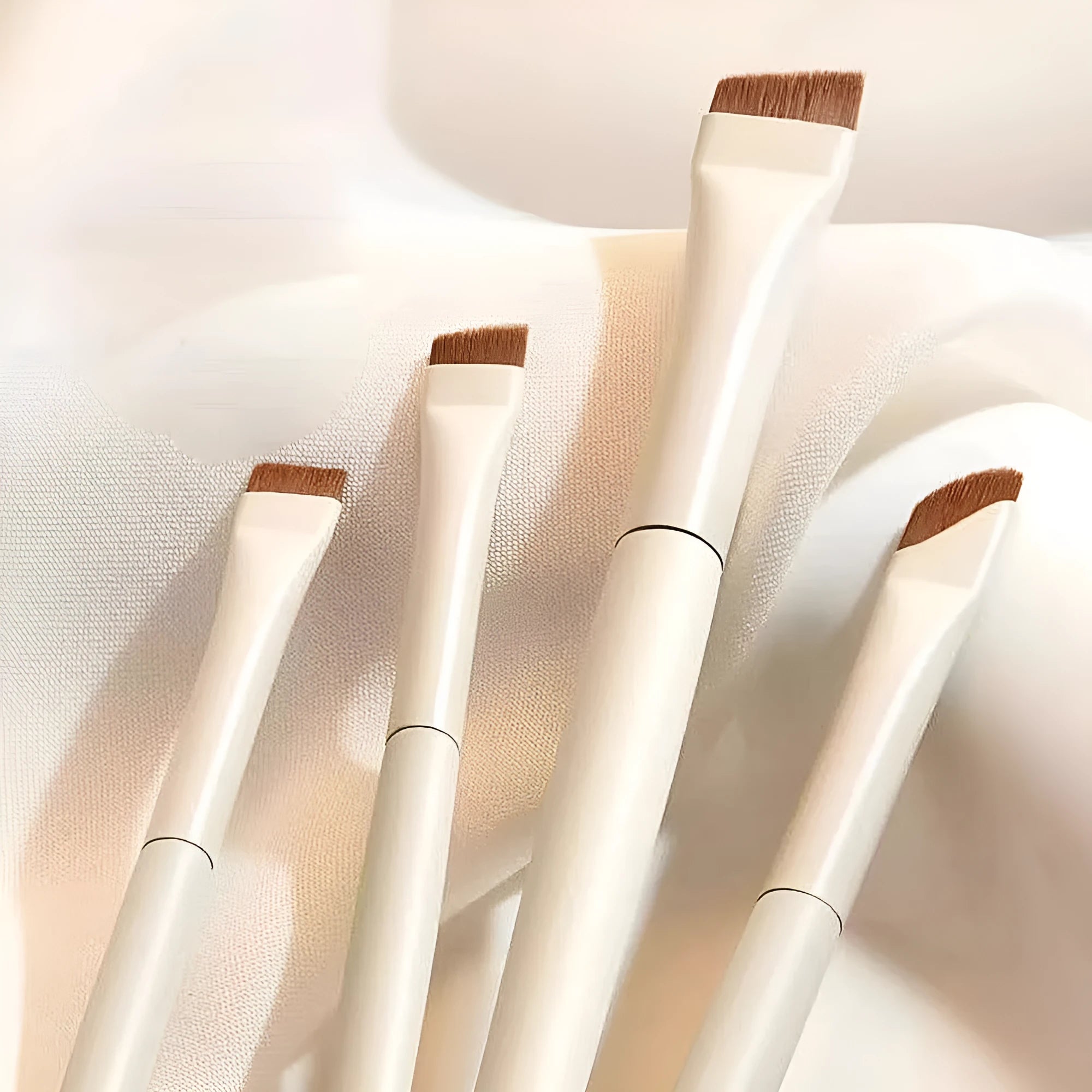 Four angled eyeliner and brow brushes with fine tips next to a leather case.