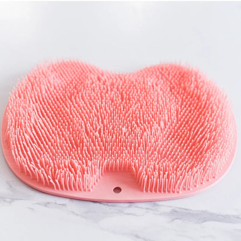 Orange suction cup bath brush with silicone bristles for foot and back cleaning on a bathroom floor.