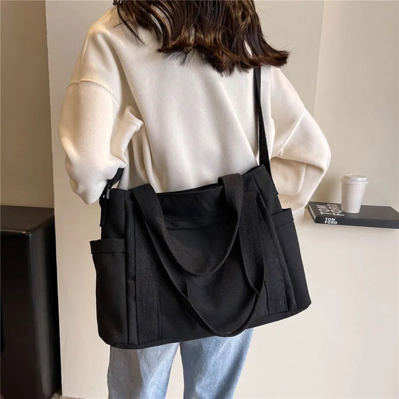 Large black polyester canvas shoulder tote bag showing outer sandwich pocket.