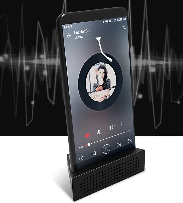 A small, coloured ABS plastic phone amplifier holder on a desktop, holding a mobile phone horizontally.