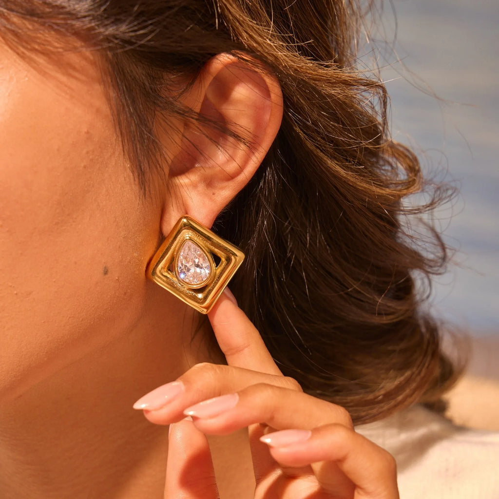 Gold geometric stud earrings with inlaid water drop zircon on white background.