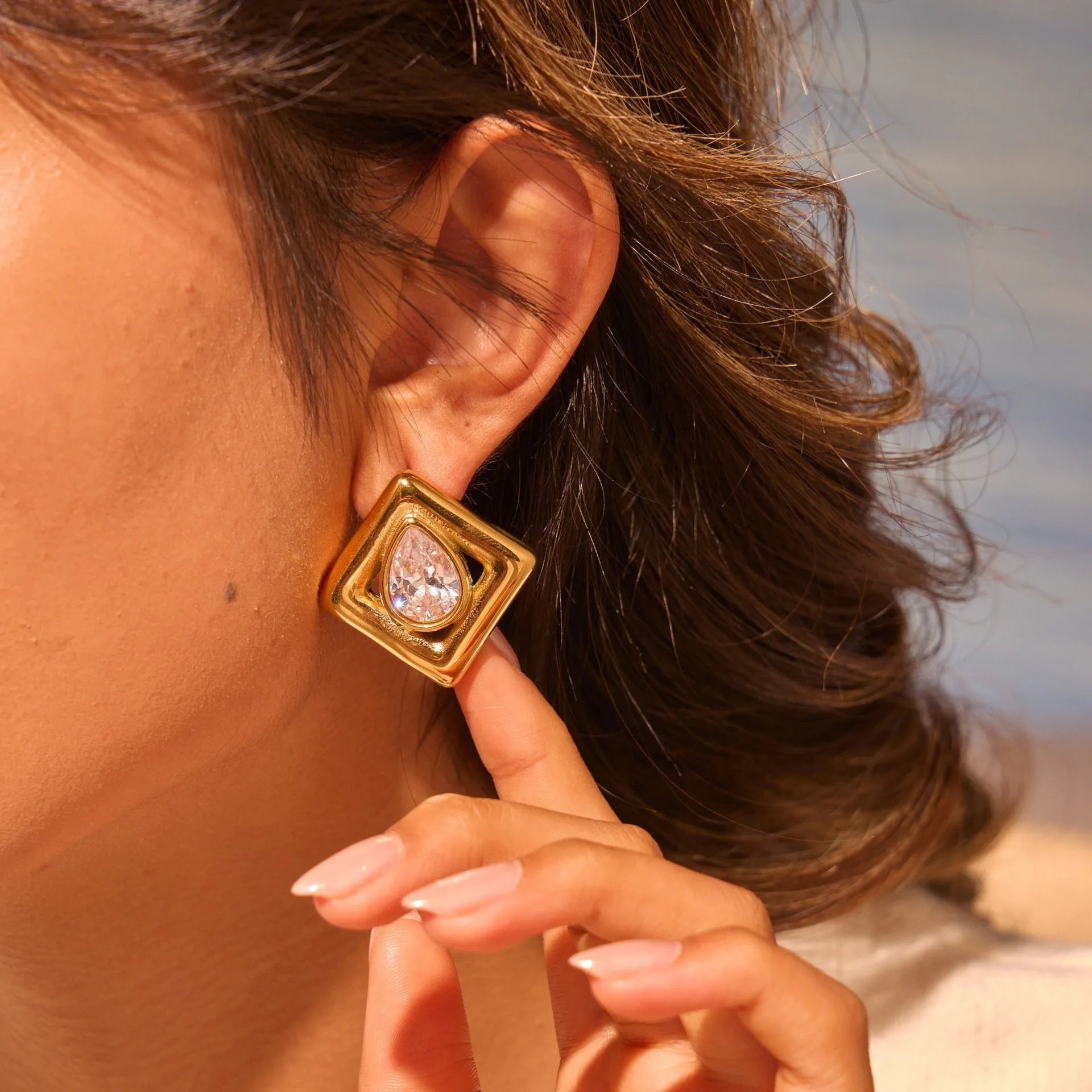 Gold geometric stud earrings with inlaid water drop zircon on white background.