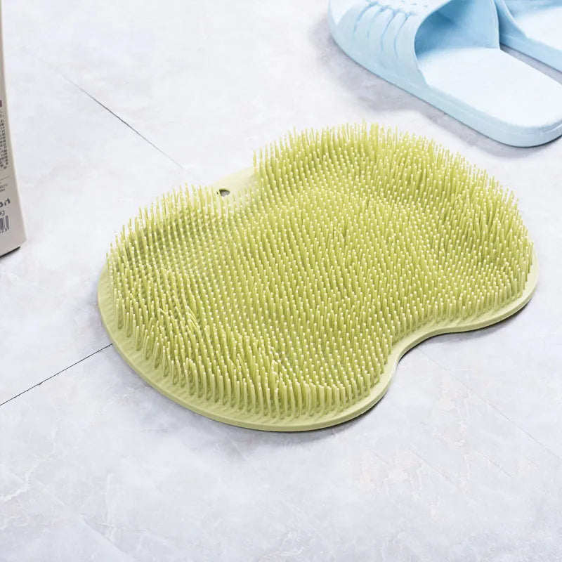Orange suction cup bath brush with silicone bristles for foot and back cleaning on a bathroom floor.