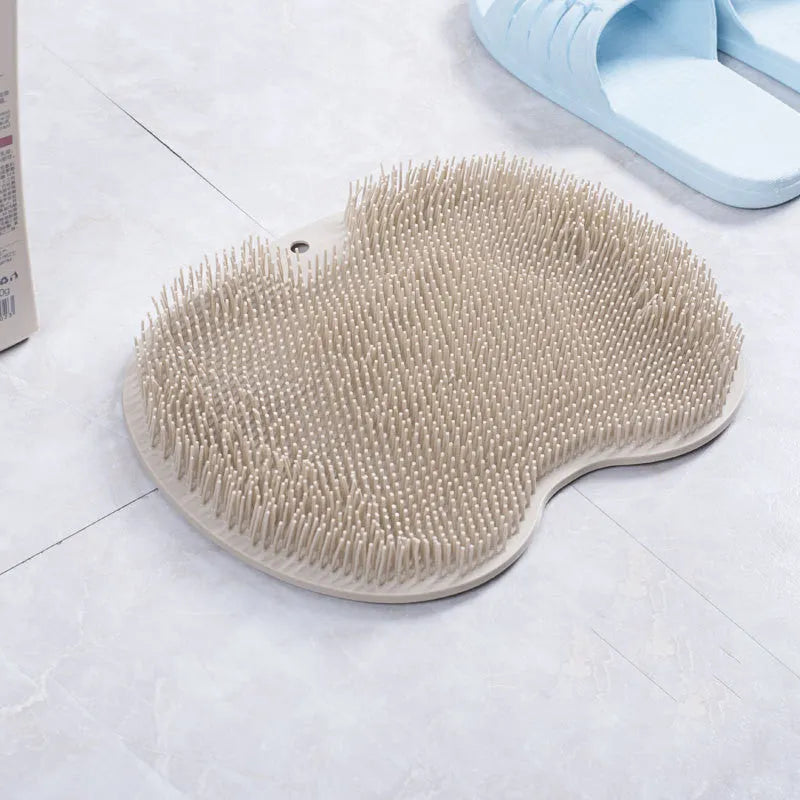 Orange suction cup bath brush with silicone bristles for foot and back cleaning on a bathroom floor.