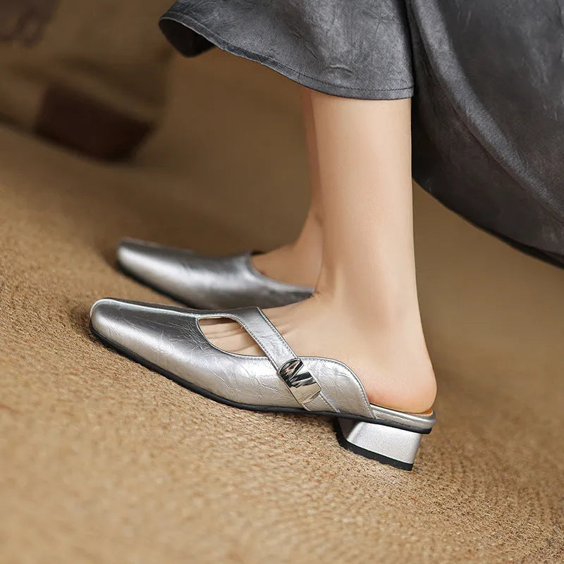 A pair of beige square head low heel slippers with a rubber sole on a wooden deck.