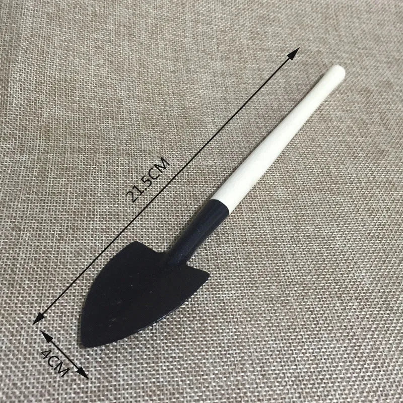 Succulent gardening tool set showing mini shovel, watering can, tweezers, and small scissors on a table.