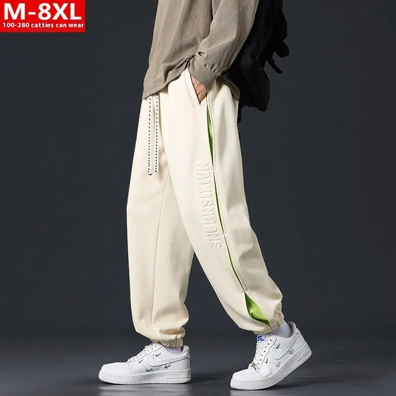 Man wearing loose grey-green cotton trousers with banded ankles and stitching detail.