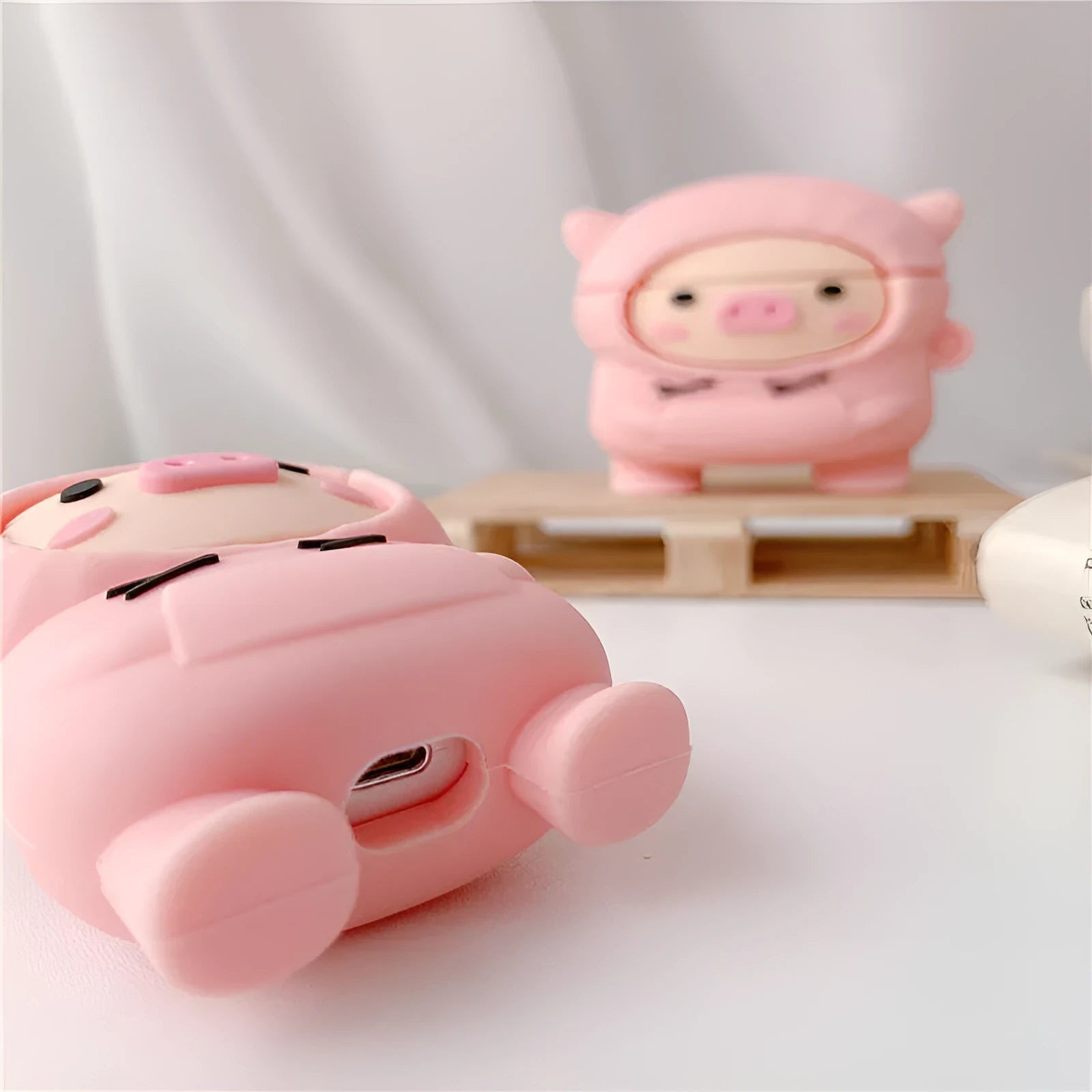 Soft pink silicone AirPods case cover with a cartoon pig graphic and a matching metal carry hook.
