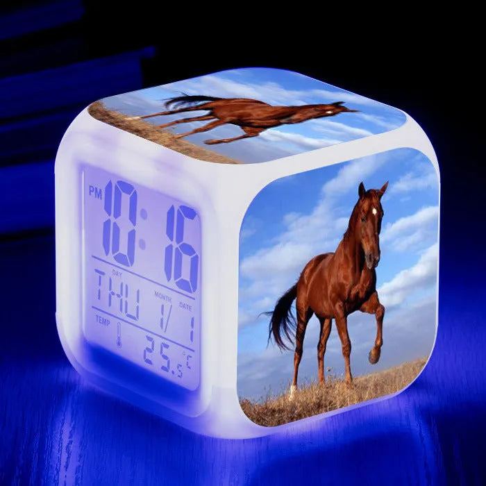 Square cartoon-style LED digital alarm clock showing time and temperature on a desk.