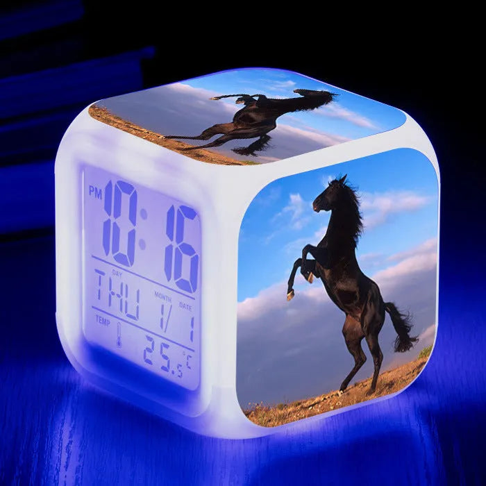 Square cartoon-style LED digital alarm clock showing time and temperature on a desk.