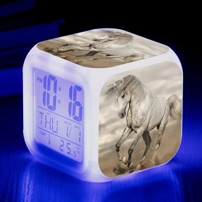 Square cartoon-style LED digital alarm clock showing time and temperature on a desk.