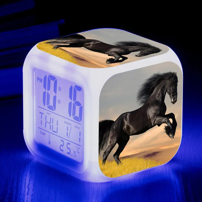 Square cartoon-style LED digital alarm clock showing time and temperature on a desk.