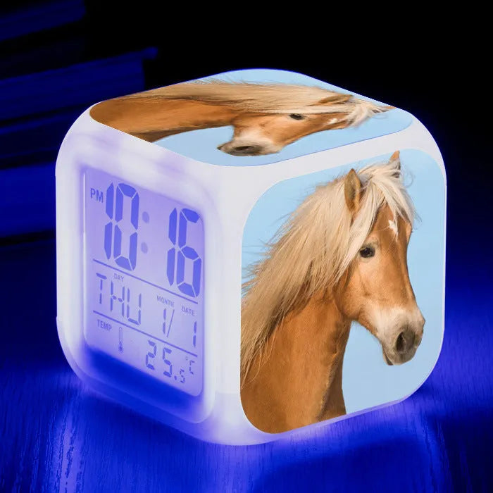 Square cartoon-style LED digital alarm clock showing time and temperature on a desk.