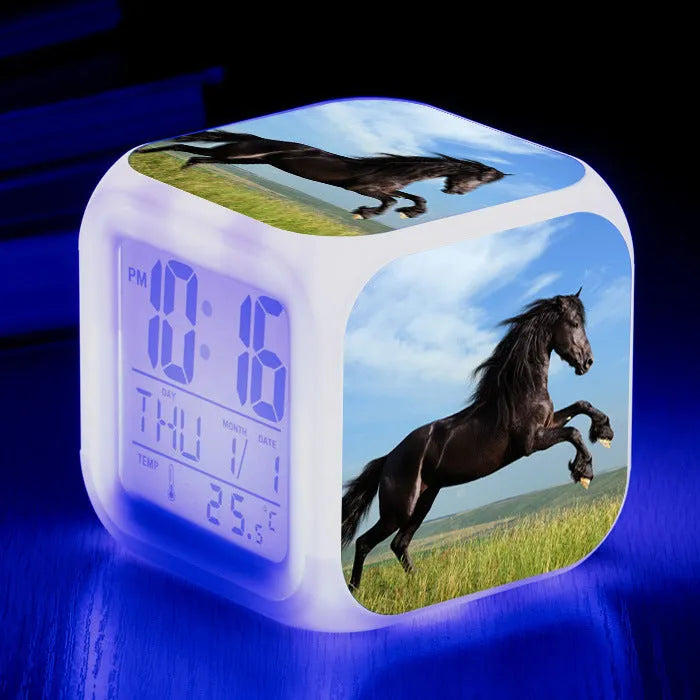 Square cartoon-style LED digital alarm clock showing time and temperature on a desk.