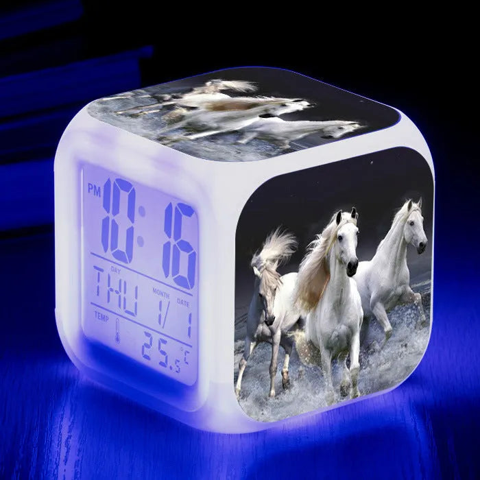 Square cartoon-style LED digital alarm clock showing time and temperature on a desk.