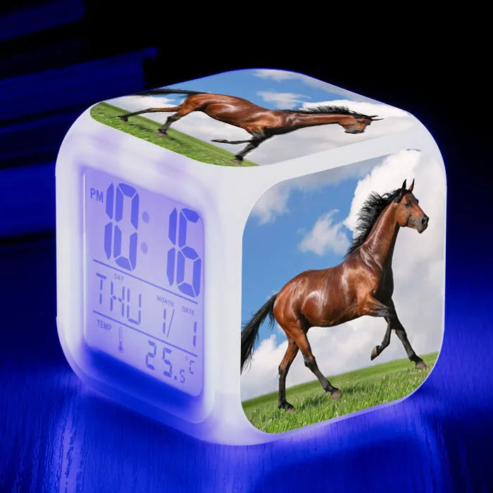 Square cartoon-style LED digital alarm clock showing time and temperature on a desk.