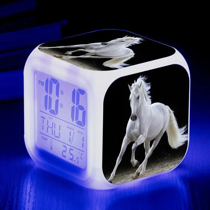 Square cartoon-style LED digital alarm clock showing time and temperature on a desk.