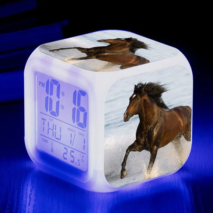 Square cartoon-style LED digital alarm clock showing time and temperature on a desk.