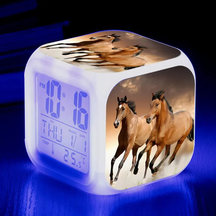 Square cartoon-style LED digital alarm clock showing time and temperature on a desk.
