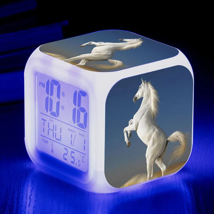 Square cartoon-style LED digital alarm clock showing time and temperature on a desk.