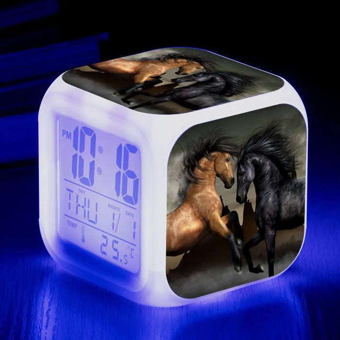 Square cartoon-style LED digital alarm clock showing time and temperature on a desk.