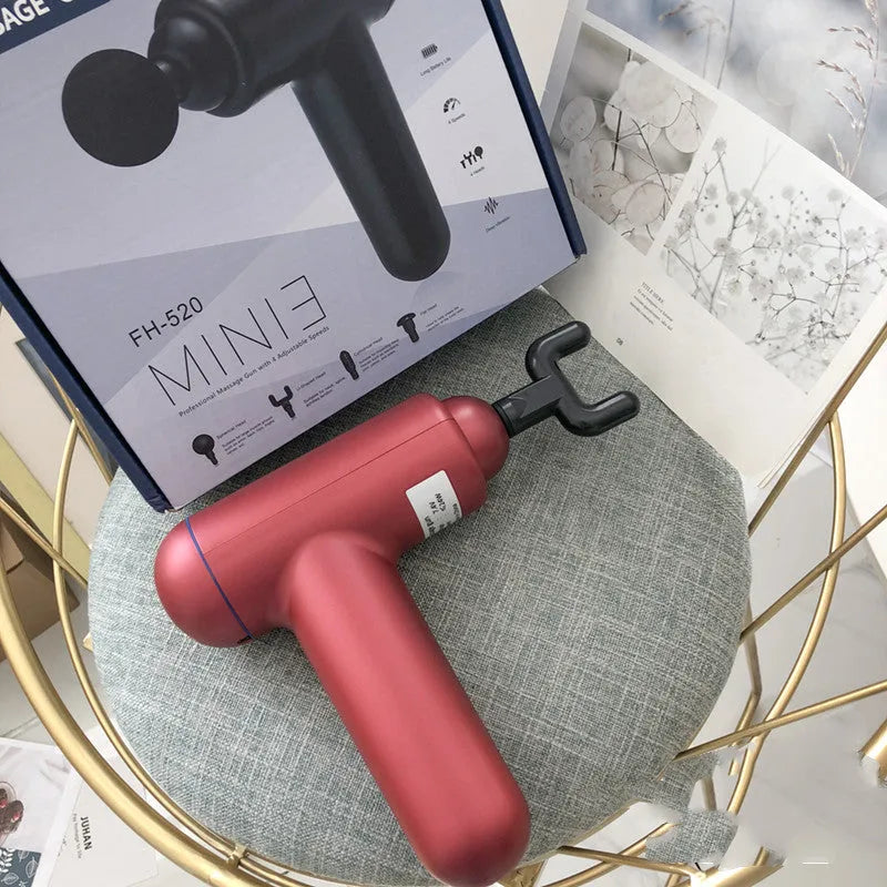 Black handheld fascia gun massager with USB port on a grey background.