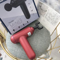 Black handheld fascia gun massager with USB port on a grey background.