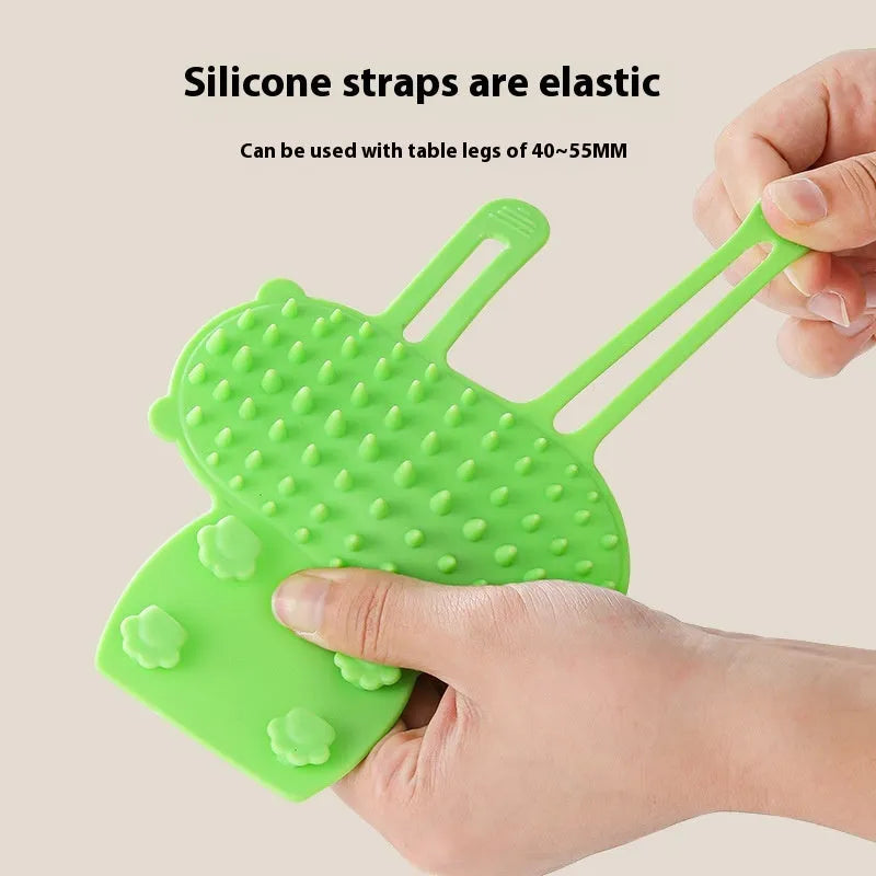 Silicone cat grooming comb with adjustable strap fastened to a table leg for self-cleaning