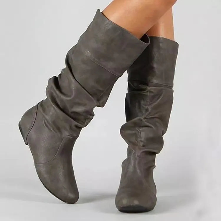 Women's flat slip-on long boots with round toe in black, shown on a foot.