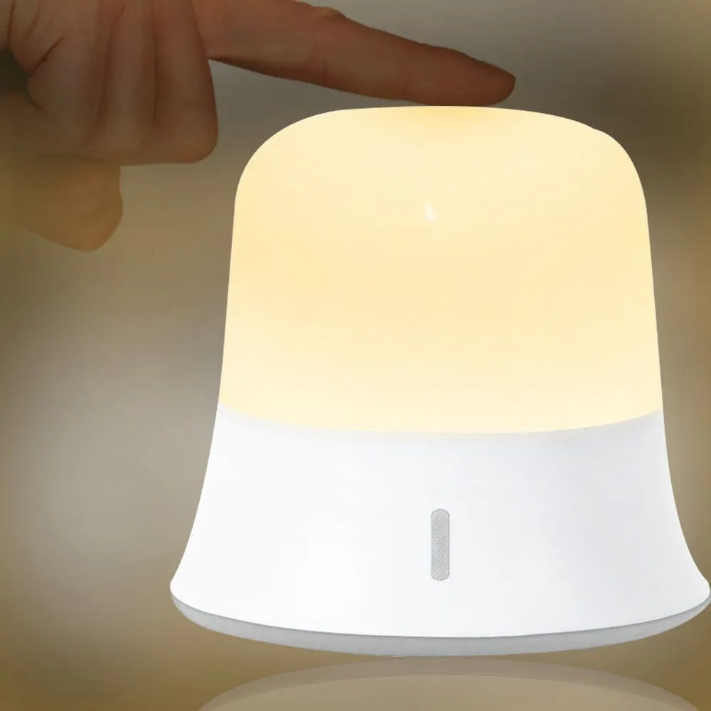 White cylindrical bedside night light with touch controls and motion sensor on a table.