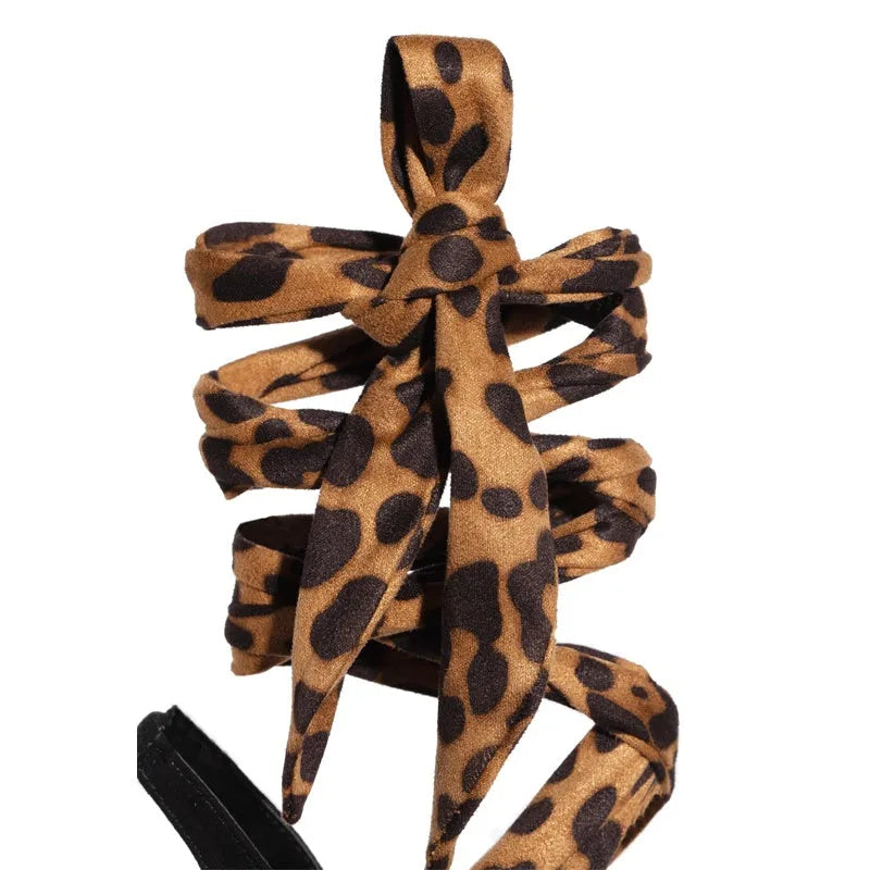 Light brown leopard print women's high heel sandals with cross-straps and a tall fine heel on a rubber sole.