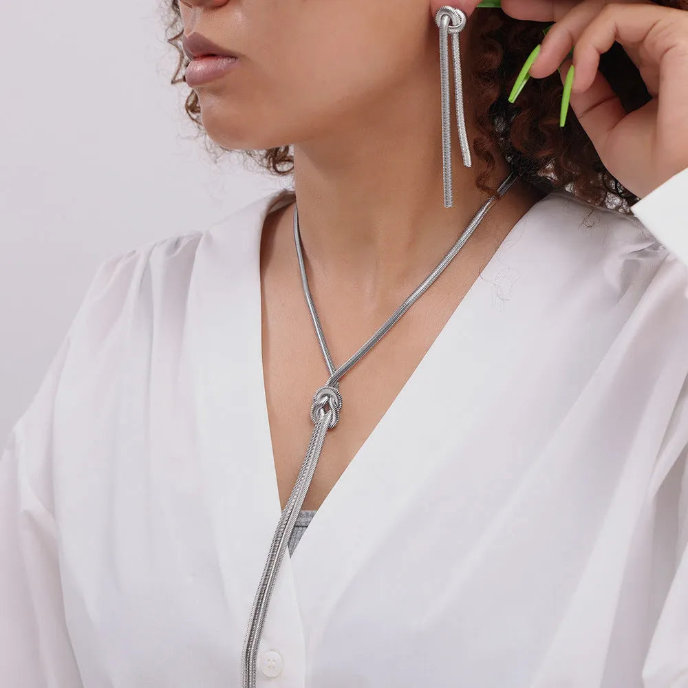 Gold titanium steel long necklace with knotted tassel pendant and matching earrings on a white background.