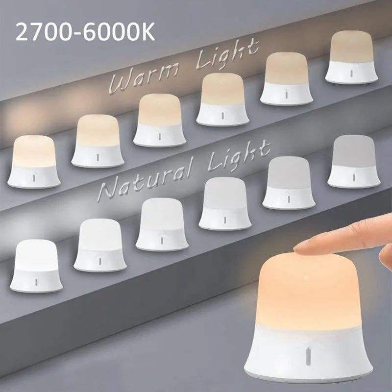 White cylindrical bedside night light with touch controls and motion sensor on a table.