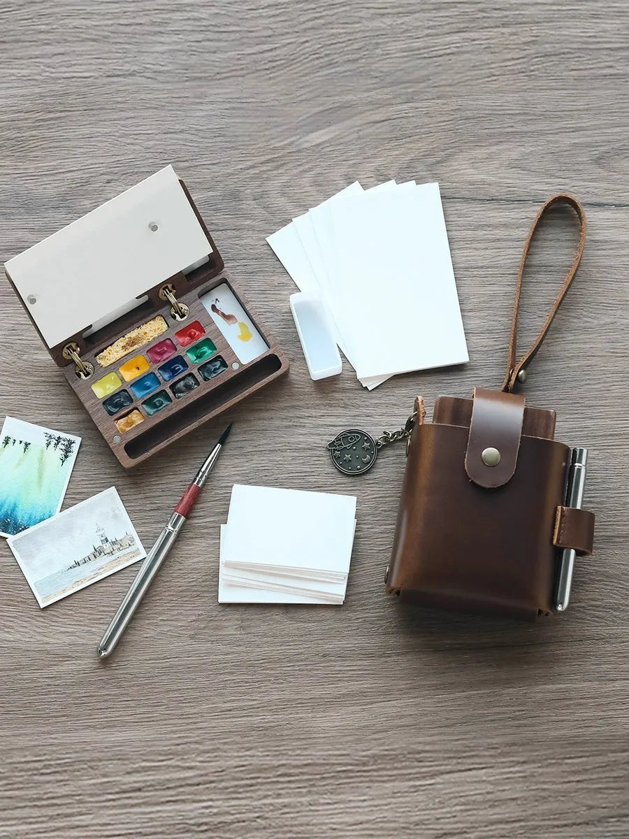 Mini walnut wooden watercolour paint box set with leather carry case, open to show professional artist pigments.