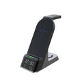 Black six-in-one wireless charging alarm clock station on a desk next to a phone and smartwatch.