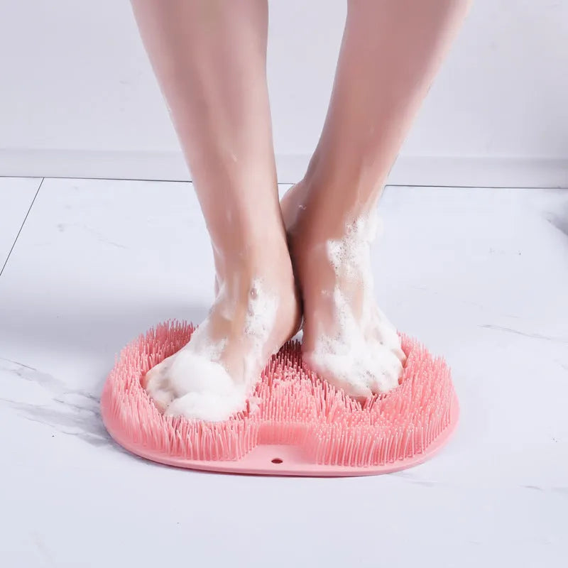 Orange suction cup bath brush with silicone bristles for foot and back cleaning on a bathroom floor.