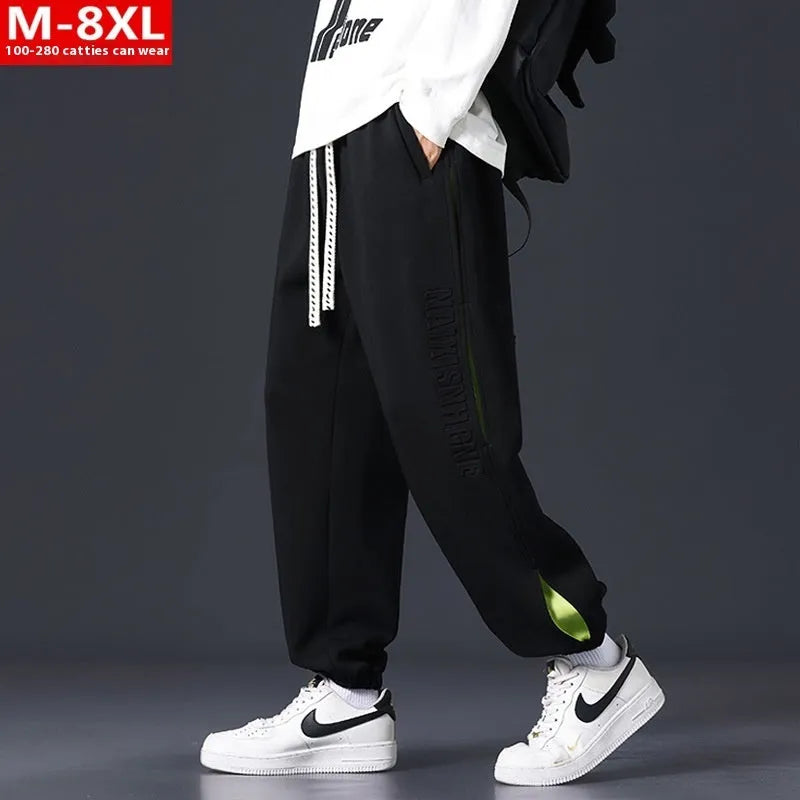 Man wearing loose grey-green cotton trousers with banded ankles and stitching detail.