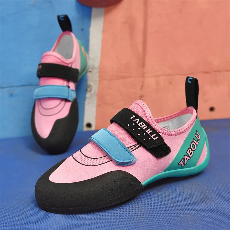 Beginner rock climbing shoes with Velcro strap in black and red colour scheme on a rocky surface.