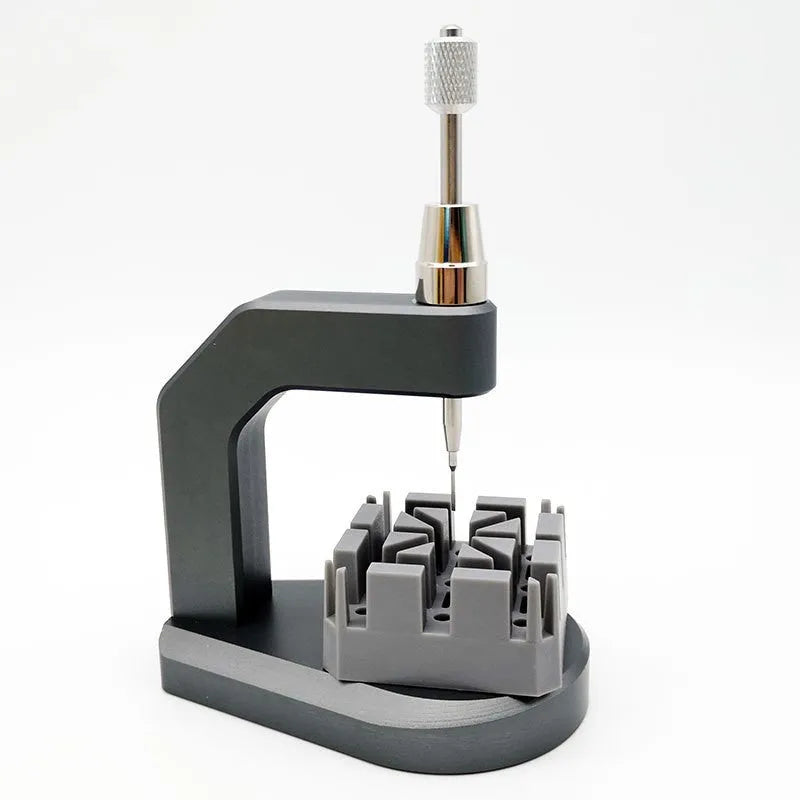 Silver coloured tool steel press strap removal tool for watch and jewellery repair on a dark surface.