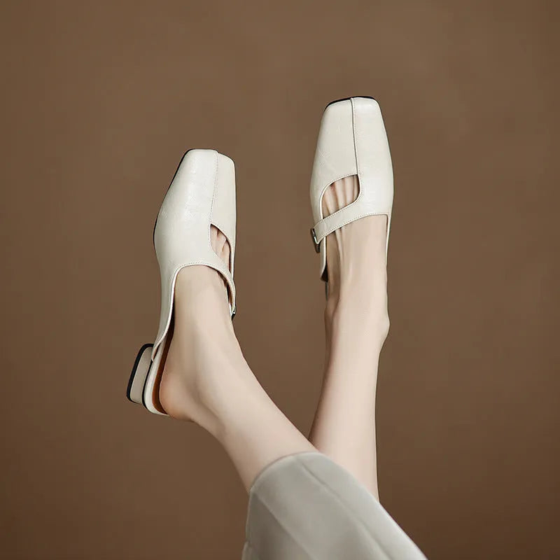 A pair of beige square head low heel slippers with a rubber sole on a wooden deck.