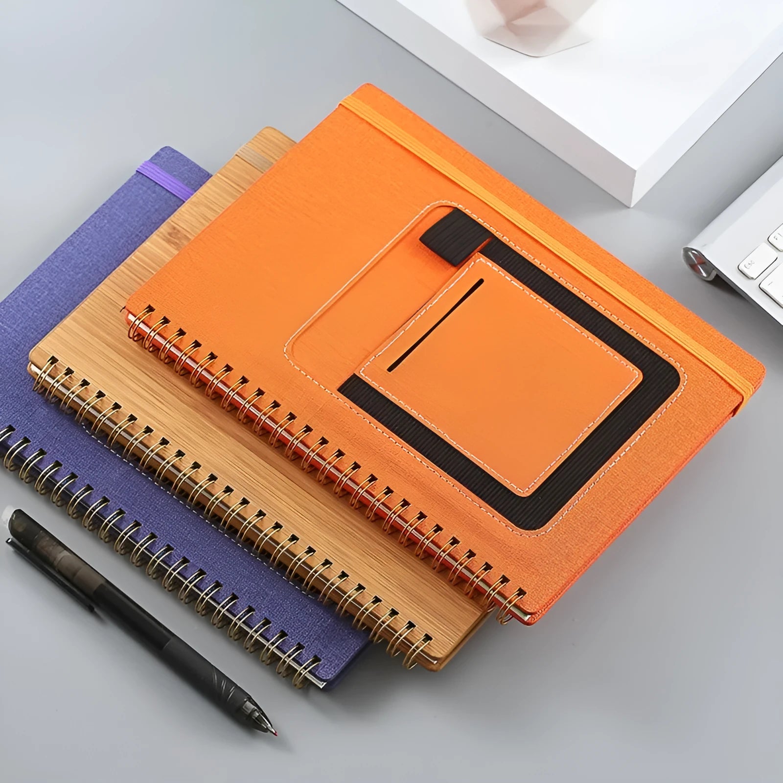 Erasable coil-bound notebook with customisable coloured cover on thick, reusable rock paper, shown with a pen.